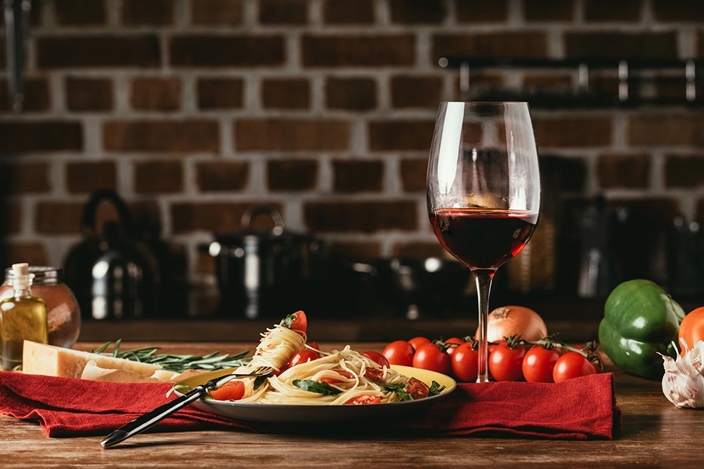 Una tavola imbandita. In primo piano, un patto di spaghetti e un calice di vino rosso.